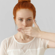 Young female redhead with her hand over her mouth.