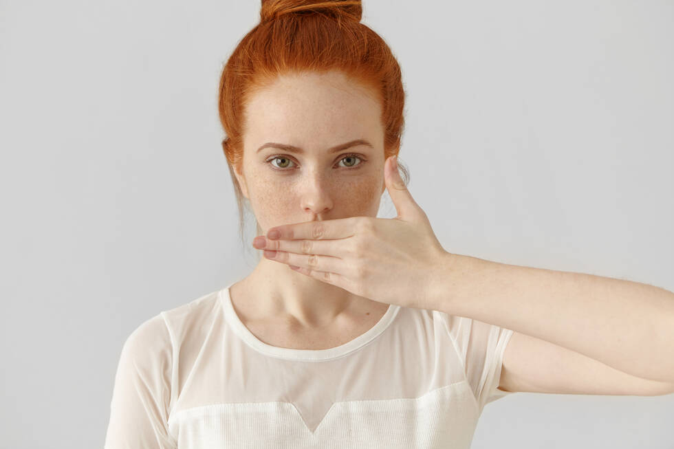Young female redhead with her hand over her mouth.