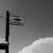 B&W photo of a lamp-post with a 'self-parking' sign that also has a drawing of a spaceship on it.