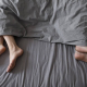 The feet of a couple in poking out from the duvet of the bottom of a bed, facing away from each other.