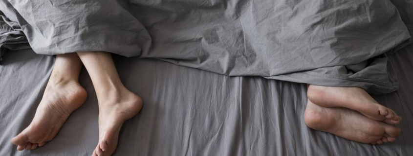 The feet of a couple in poking out from the duvet of the bottom of a bed, facing away from each other.