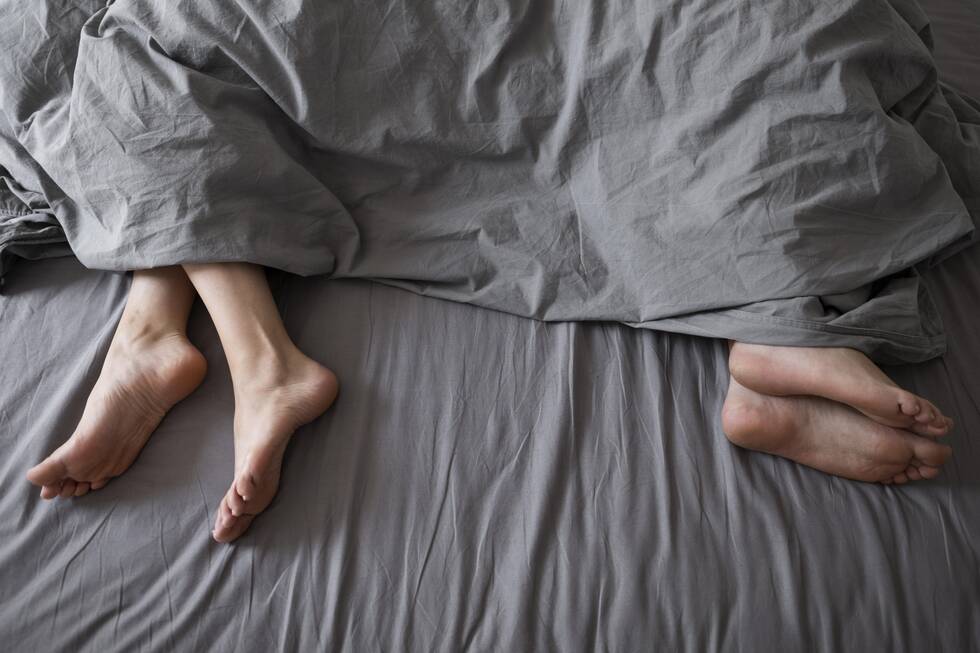 The feet of a couple in poking out from the duvet of the bottom of a bed, facing away from each other.
